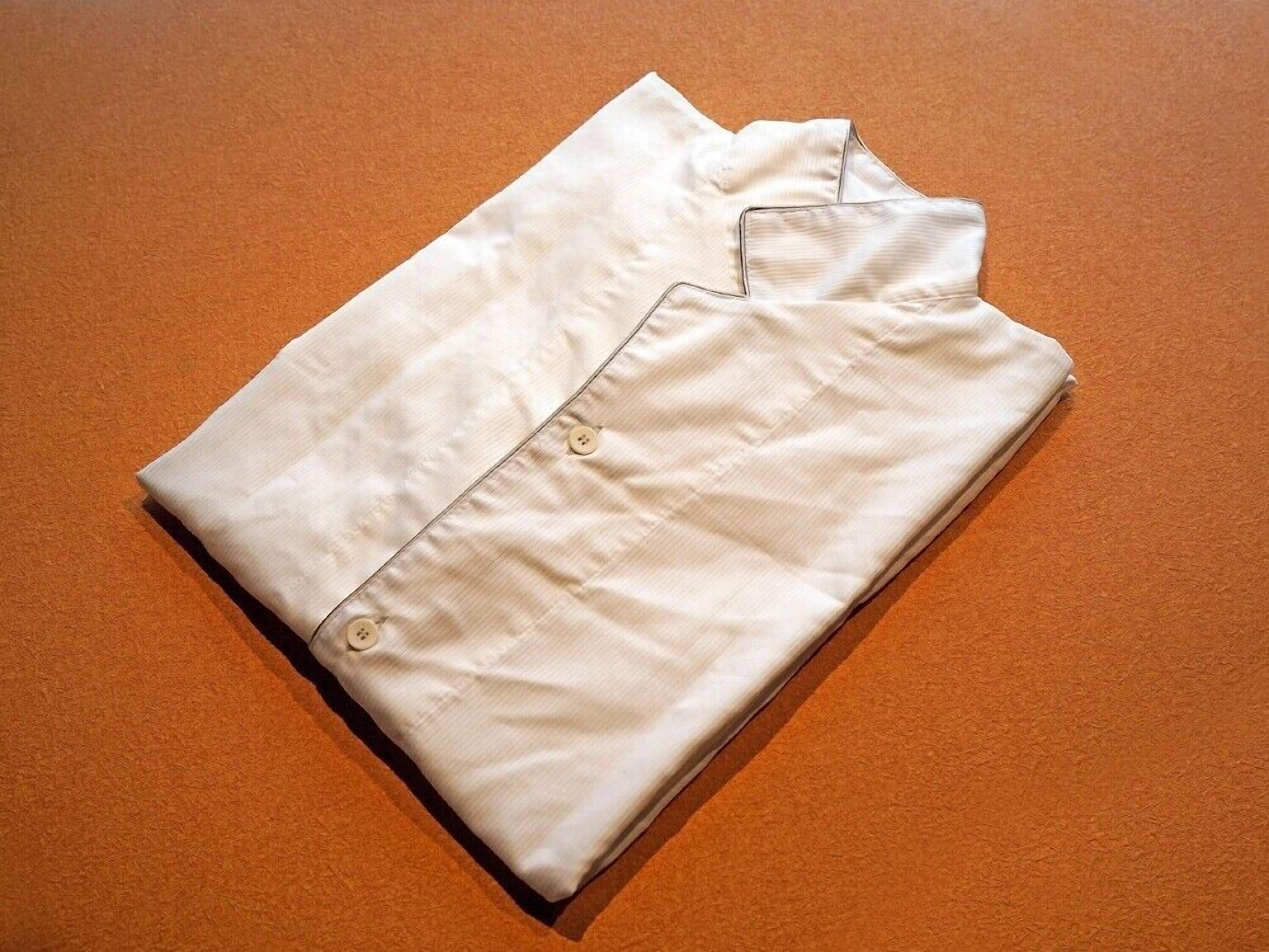 A neatly folded white shirt with buttons on an orange textured surface.