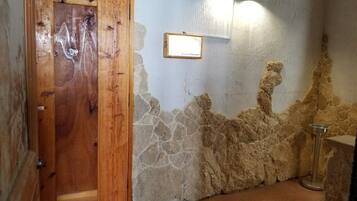 Una habitación con puerta de madera, pared de piedra, lámpara de metal y una pequeña mesa.