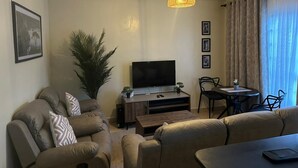 A living room with a TV, sofa, coffee table, and a dining area with chairs and a table.