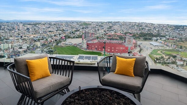 Terraza en la azotea con dos sillones grises y una mesa redonda con una chimenea, con vistas a un paisaje urbano.