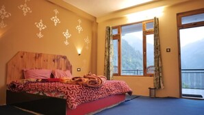 A bedroom with a wooden headboard, a bed with patterned bedding, a window with curtains, and a view of mountains. - Yellowjackets Hotel Tosh (Tosh)
