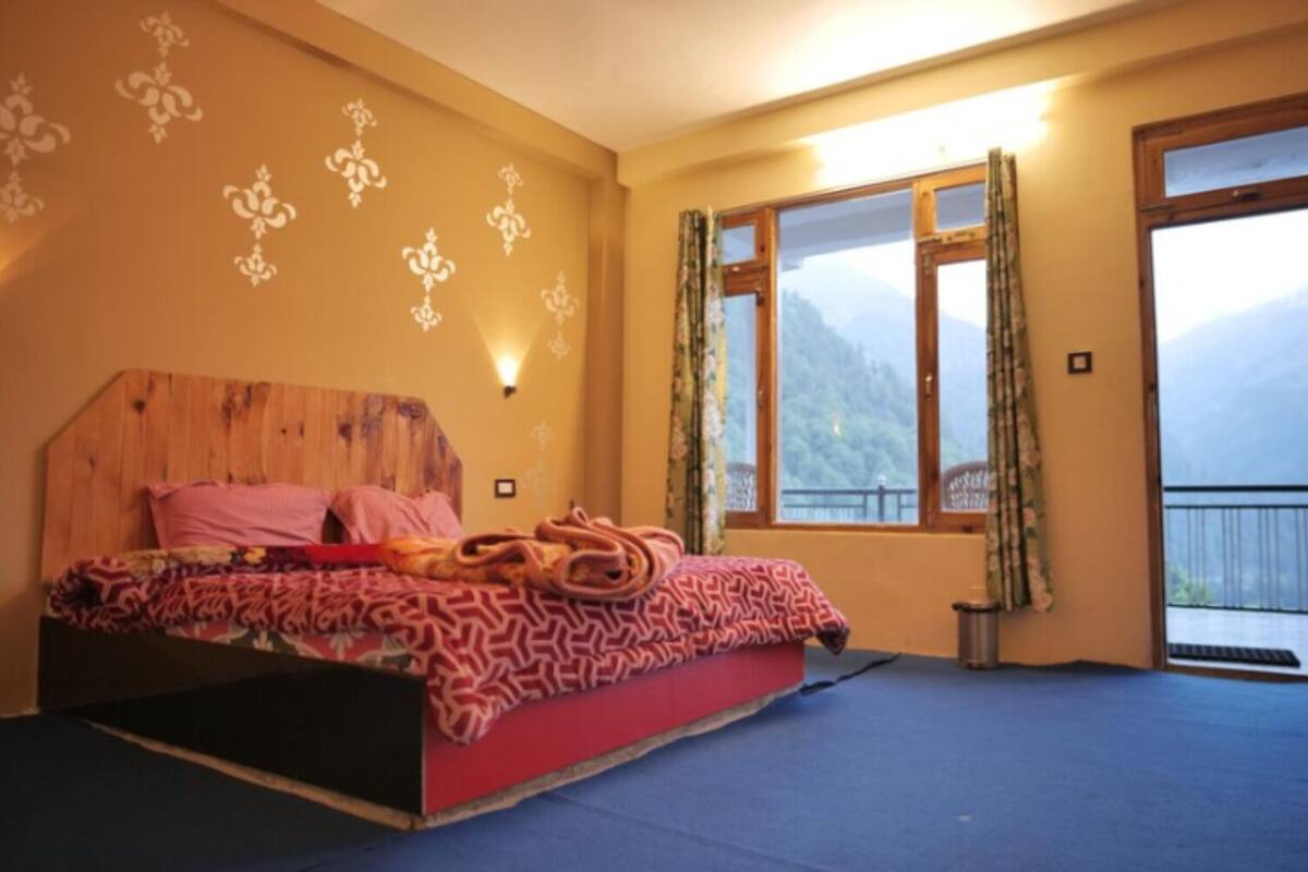 Un dormitorio con cabecera de madera, cama con ropa de cama estampada, ventana con cortinas y vistas a montañas.