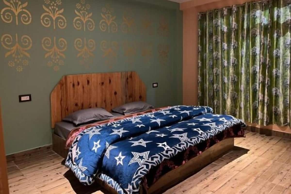 Un dormitorio con cabecera de madera, cama con colcha de rayas azules y blancas, y pared verde con papel tapiz floral.