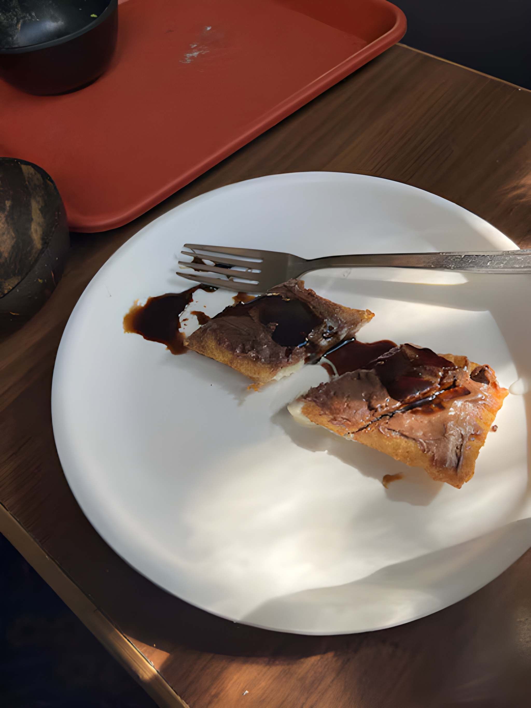 Une assiette blanche avec un morceau de nourriture et une fourchette, posée sur une table en bois.