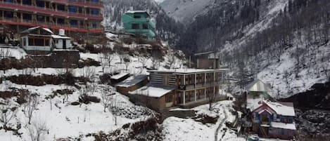 A mountainous area with buildings, including a multi-story hotel and smaller structures, amidst snow-covered terrain.