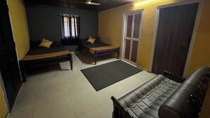 A room with two beds, a sofa, a ceiling fan, and a sliding door. - Olive Garden (Valparai)