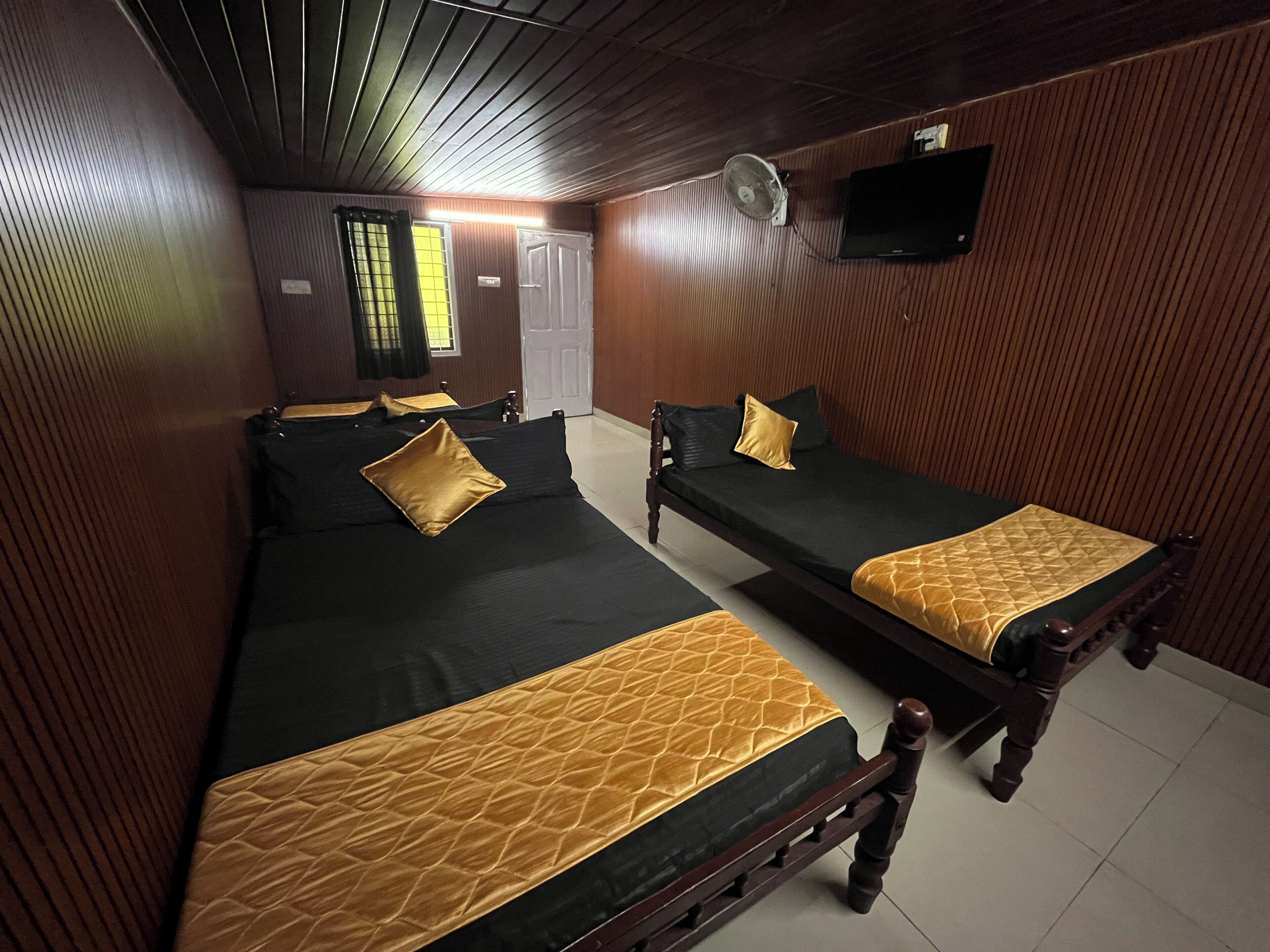 A hotel room with two single beds, a wooden ceiling, a wall-mounted TV, and a door with a window.