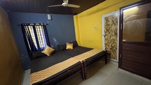 A room with a bed, a ceiling fan, a window with curtains, and a door with a decorative panel. - Olive Garden (Valparai)