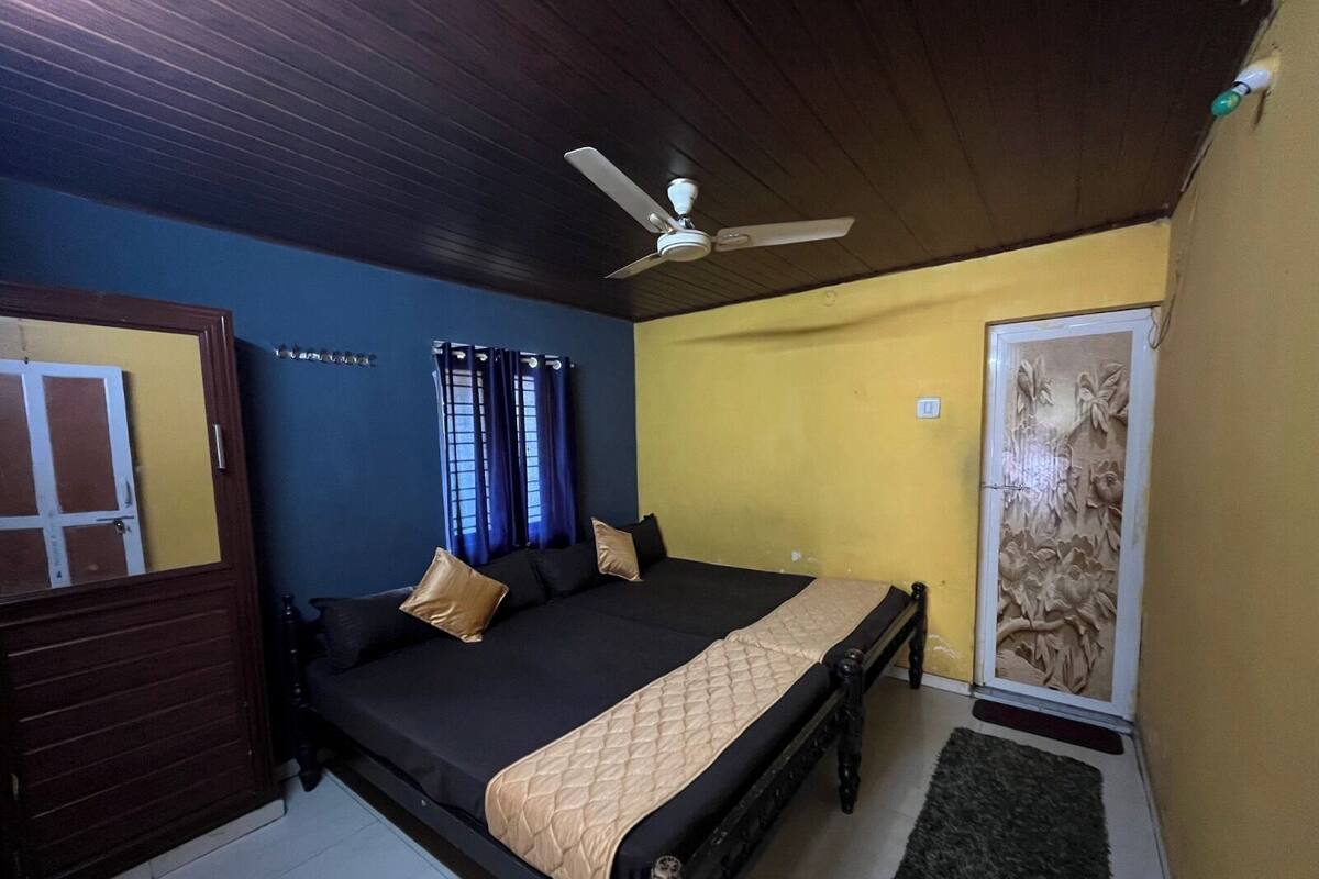 Une chambre à coucher avec un lit, un ventilateur de plafond, une porte et un mur orné d’un motif floral.