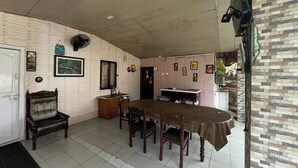 A dining area with a long table, chairs, a sofa, and a fan. - Olive Garden (Valparai)