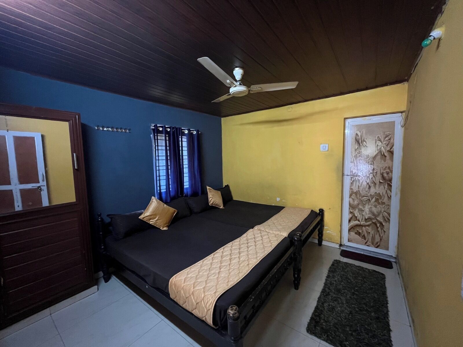 A bedroom with a bed, a ceiling fan, a door, and a wall with a floral design.