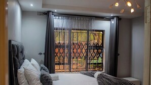 A bedroom with a bed, a headboard, a window with curtains, and a view of the outdoors. - Chishongo residence, your peaceful Darwendale getaway (Zvimba)