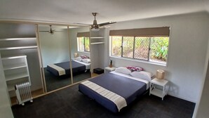 A bedroom with a large bed, a wardrobe, a mirror, a window with a view of greenery, and a ceiling fan. - Relaxing country home half way between Gold Coast and Brisbane (Wolffdene)