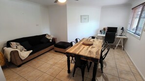 Una sala de estar con un sofá, una mesa de comedor con sillas, una mesita con un florero y un televisor sobre un mueble.