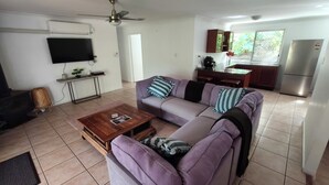 A living room with a sofa, coffee table, TV, and kitchen area with a refrigerator. - Relaxing country home half way between Gold Coast and Brisbane (Wolffdene)