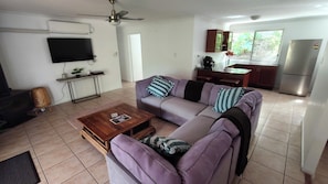 Una sala de estar con sofá, mesa de centro, televisor y una zona de cocina con refrigerador.