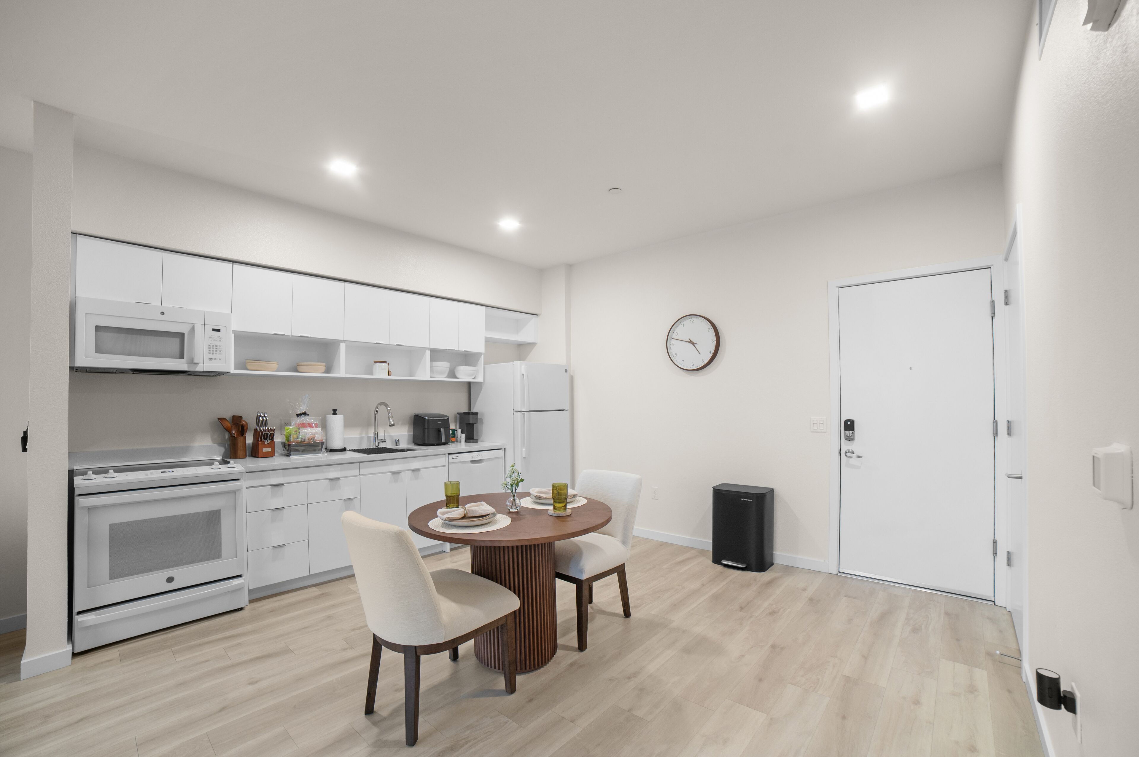 A modern kitchen with white cabinets, a microwave, stove, and a dining area with two chairs and a table.
