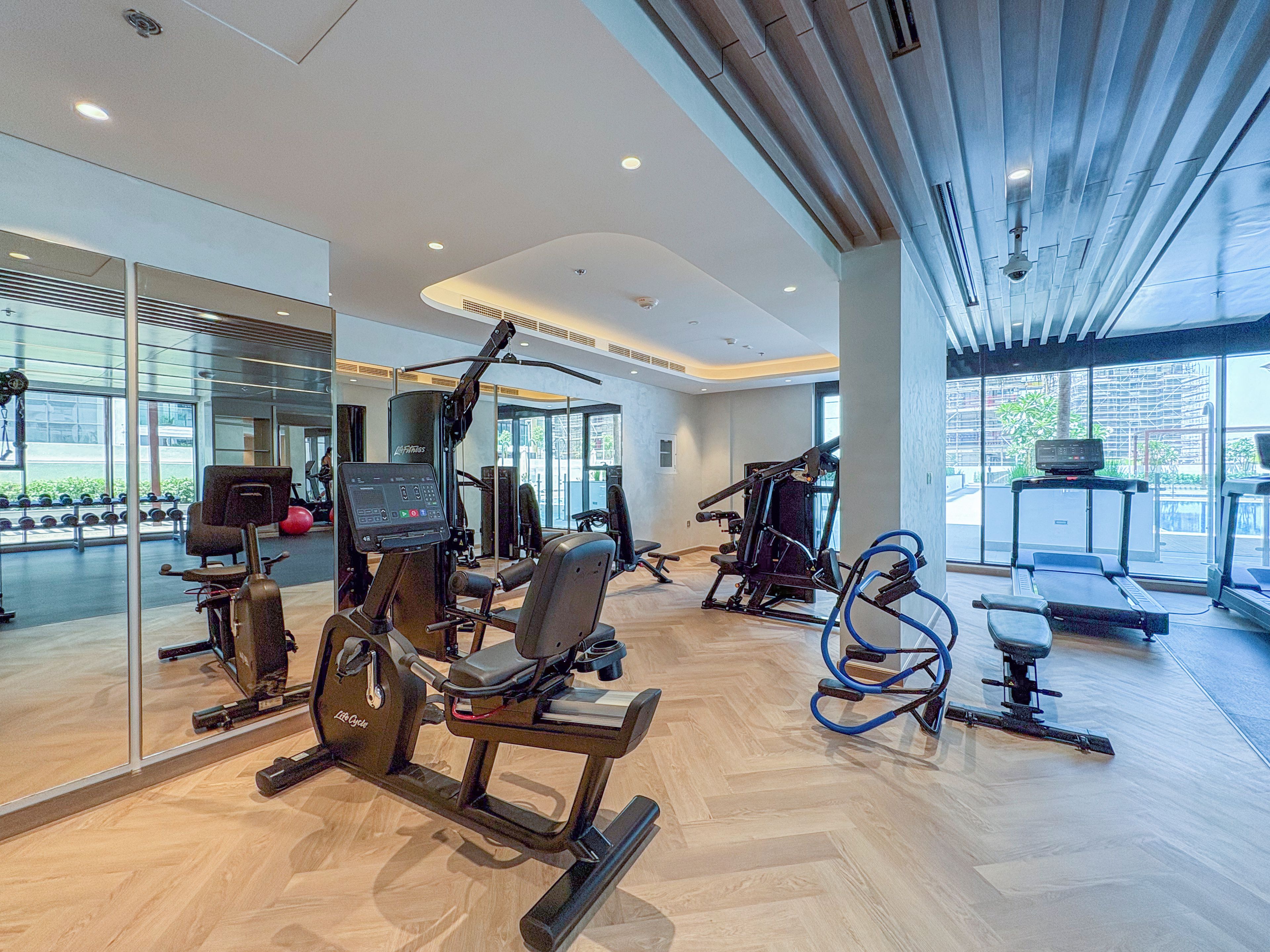 A modern gym with various exercise equipment, large windows, and a herringbone floor pattern.