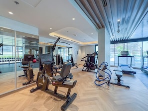 A modern gym with various exercise equipment, large windows, and a herringbone floor pattern. - Bloomfields Studio - Azizi Riviera 61 - Meydan (Dubai)