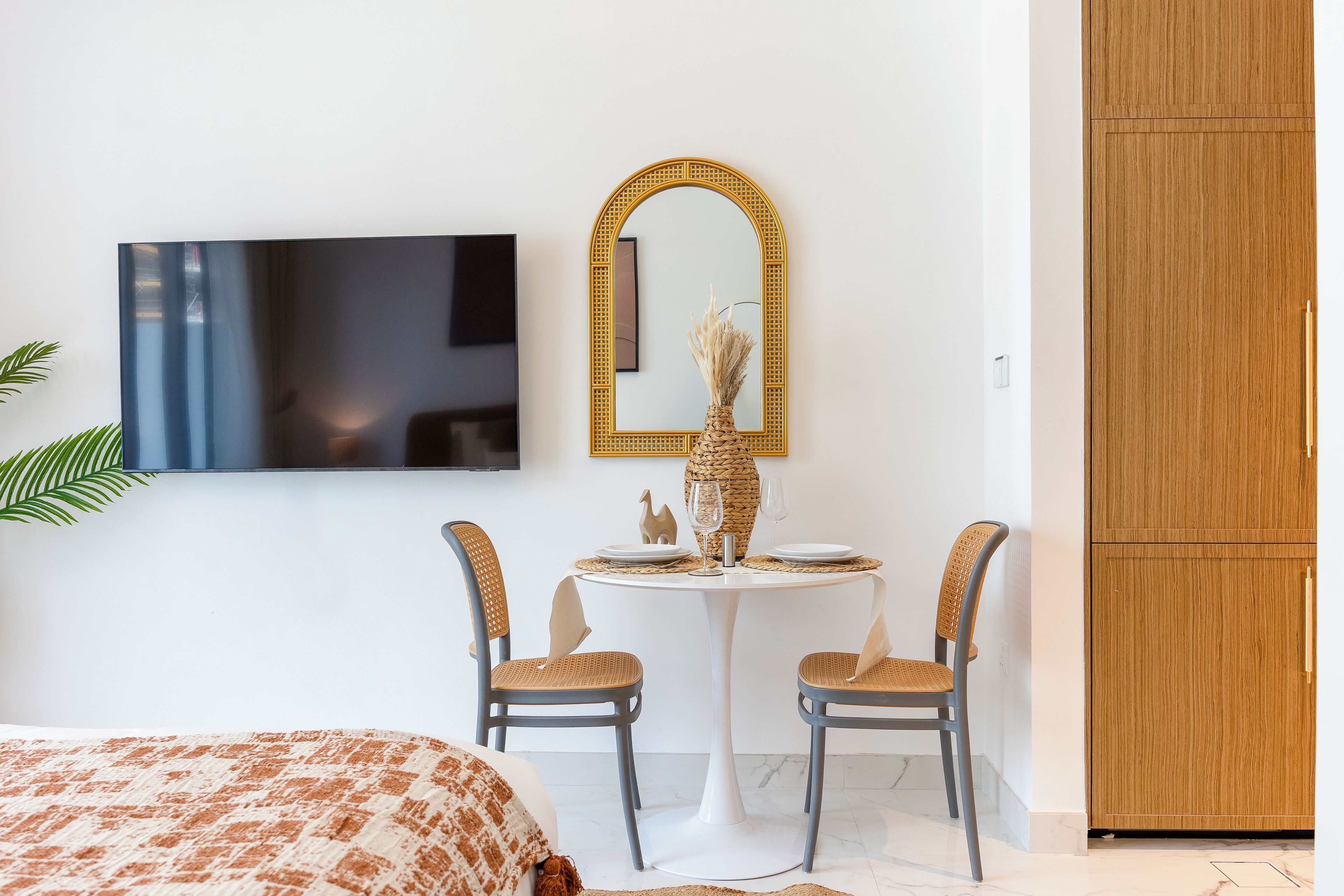 A hotel room with a bed, a TV mounted on the wall, a round dining table with chairs, and a wardrobe.