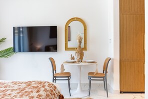 Habitación de hotel con una cama, televisor montado en la pared, una mesa redonda con sillas y un armario.
