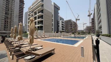 Area piscina sul tetto con lettini e ombrelloni, circondata da edifici moderni e gru da costruzione.