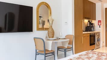 Una camera d'albergo moderna con TV a schermo piatto, un'area pranzo con due sedie e un tavolo, una cucina con macchina da caffè e lavatrice.