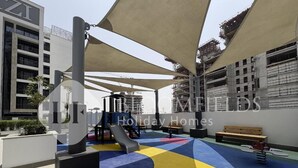 An outdoor play area with a slide, benches, and exercise equipment. - Bloomfields Elegant Stu in Azizi (Dubai)