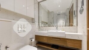 A modern bathroom with a marble vanity, a large mirror, and a toilet. - Bloomfields Elegant Stu in Azizi (Dubai)