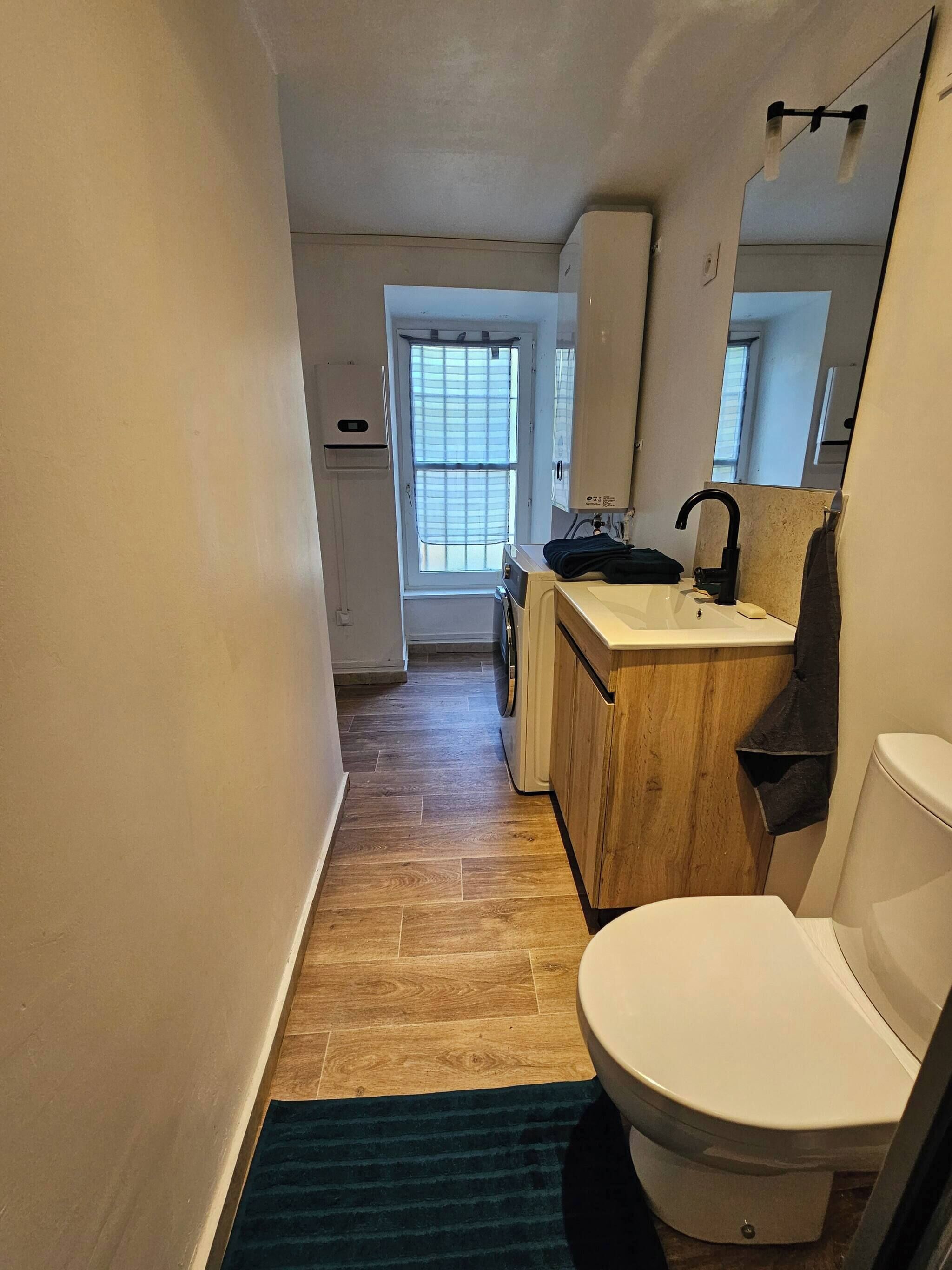 A narrow hallway leading to a bathroom with a toilet, sink, and a window.