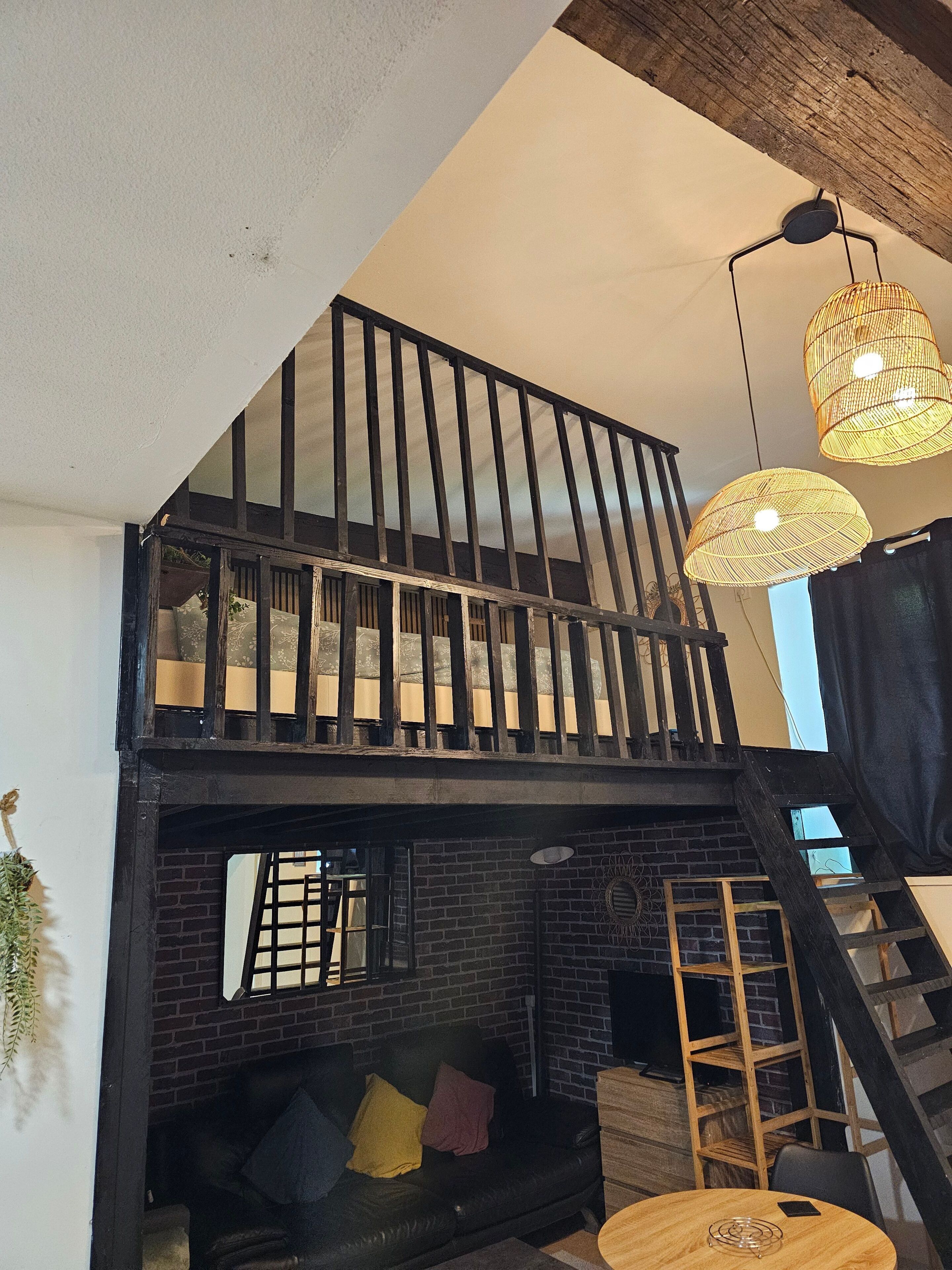 Ett rum i loftstil med en svart lädersoffa, ett träbord och en trappa.