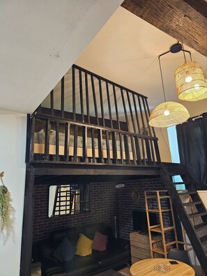 A loft-style room with a black leather sofa, a wooden table, and a staircase. - Duplex 15 min from train station, Montluçon historic center (Montluçon)