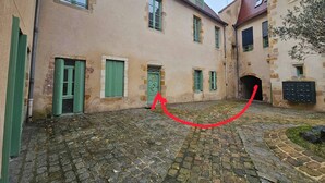 Ein Innenhof mit Kopfsteinpflaster, Steingebäude mit grünen Fensterläden und einem kleinen Bogen.