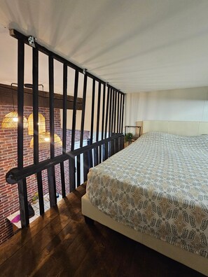 A bedroom with a bed, a wooden floor, a brick wall, and a black metal railing. - Duplex 15 min from train station, Montluçon historic center (Montluçon)