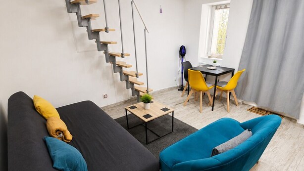 A modern living space with a staircase, a black sofa, a blue armchair, and a dining area with yellow chairs. - 35 m² duplex 8 min walk to Montluçon train station (Montluçon)