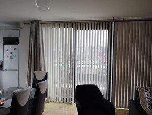 A modern living room with a dining area, featuring a large sliding glass door with vertical blinds, a refrigerator with magnets, and a black sofa. - 2 Bedroom Apartment 4-6 people-Coastal Comfort (Balbriggan)