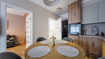 A modern kitchen with wooden cabinets, a built-in oven, and a sink. There is a dining area with a round table and four chairs.