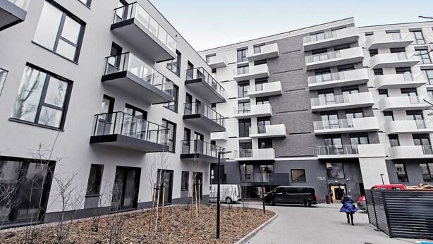 A modern multi-story residential building with balconies, a parking area, and a pedestrian pathway.