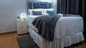 Quarto moderno com uma cama grande, uma mesinha de cabeceira e uma cortina escura.