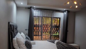 Un dormitorio con una cama grande, cabecera, ventana con vista a un jardín y una lámpara en el techo.