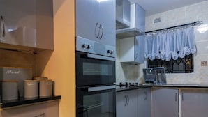 Una cocina con horno empotrado, estufa a gas y extractor. Hay armarios de almacenamiento y una encimera con un recipiente para pan.