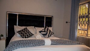 Een bed met een zwart hoofdeinde, witte beddengoed en gestreepte kussens.