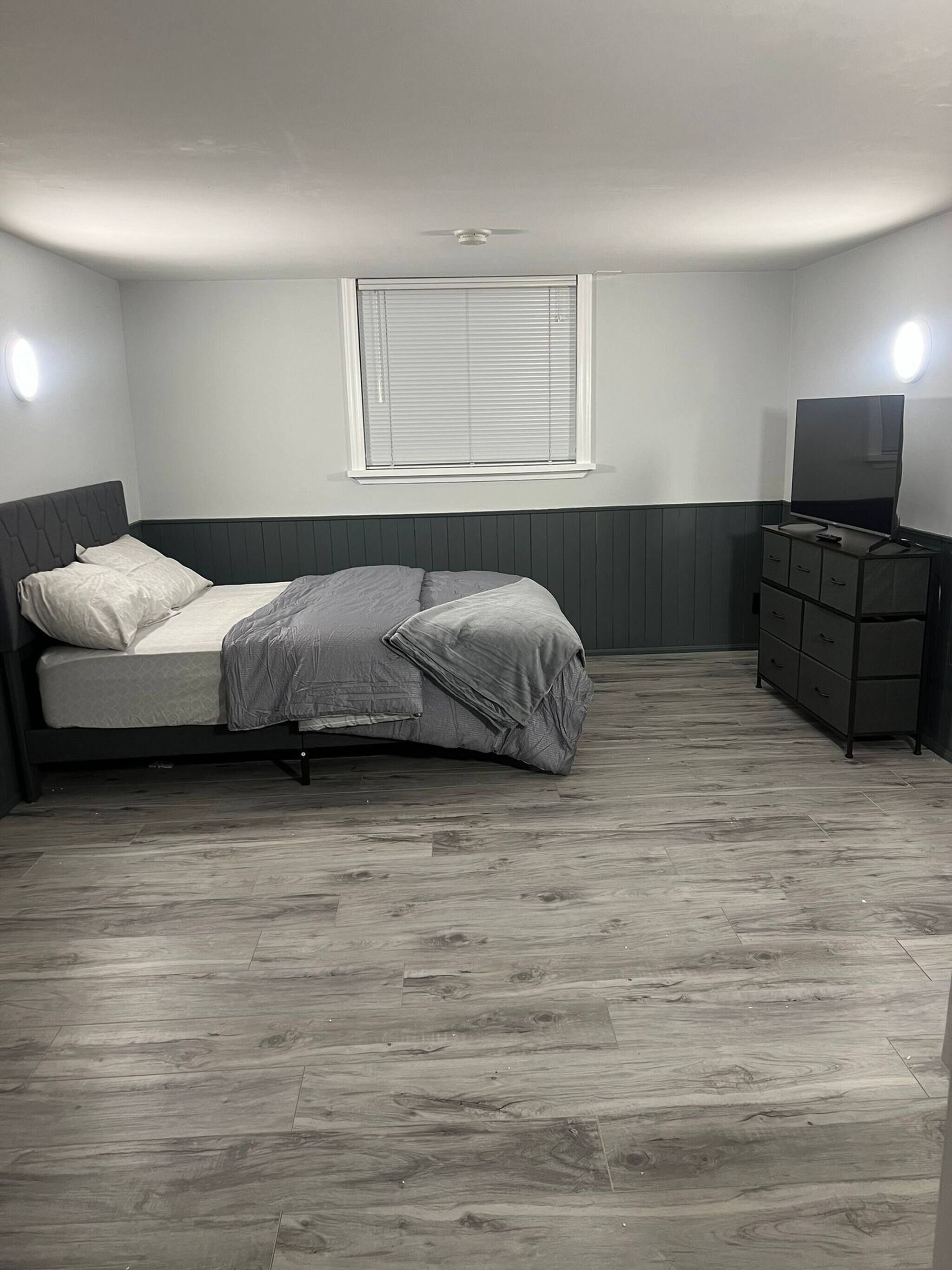 Un dormitorio con cama, cómoda, televisor y ventana con persianas.