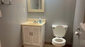 A bathroom with a toilet, a sink with a mirror above it, and cabinets. - Prime Location Studio with Separate amenities (London)