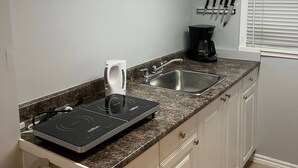 A compact kitchen with a built-in induction cooktop, a coffee maker, and a sink. - Prime Location Studio with Separate amenities (London)