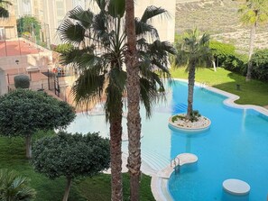 A swimming pool with palm trees and a view of a building in the background. - Ground-floor apartment overlooking the Mediterranean, with an outdoor pool and gym (El Campello)