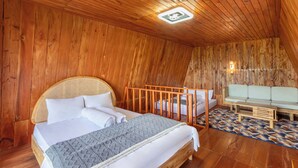 A wooden-paneled room with a bed, a crib, a sofa, and a patterned rug. - Emerald Cabin Dieng (Kejajar)