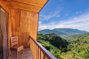 Un balcón de madera con una silla de madera, con vista a un paisaje montañoso.