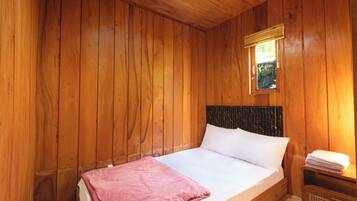 A wooden room with a bed, a window with blinds, and a small table with a towel.