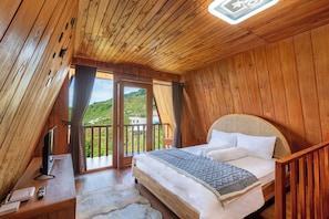 A wooden room with a bed, a TV, a desk, and a balcony with a view of greenery. - Emerald Cabin Dieng (Kejajar)
